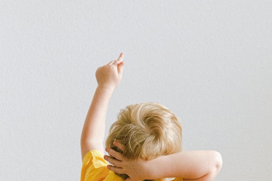Small boy in yellow shirt points up at the words 'Who I am?' on the wall. Illustrating the need for self-discovery.