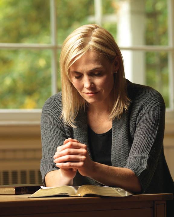 A woman praying with open scriptures in front of her. Illustrating the steps I took to avoid leaving the Mormon church and becoming ex-Mormon.