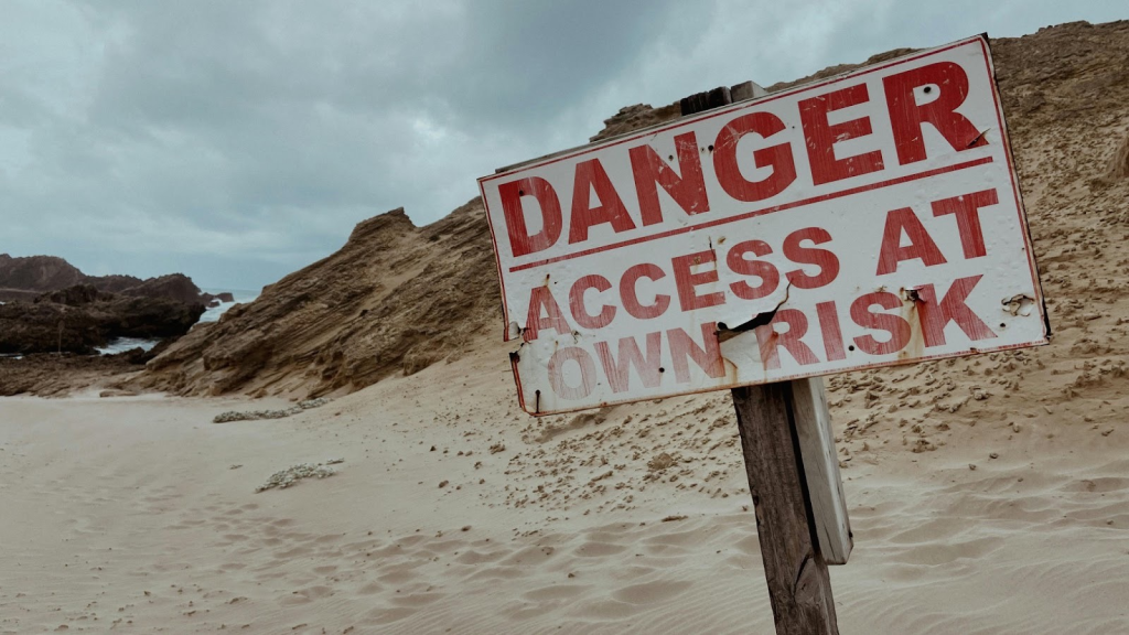 A sign in the sand that reads Danger: Access at own risk written in large red letters. Illustrating the fear I felt about ex-Mormons and leaving the LDS church.