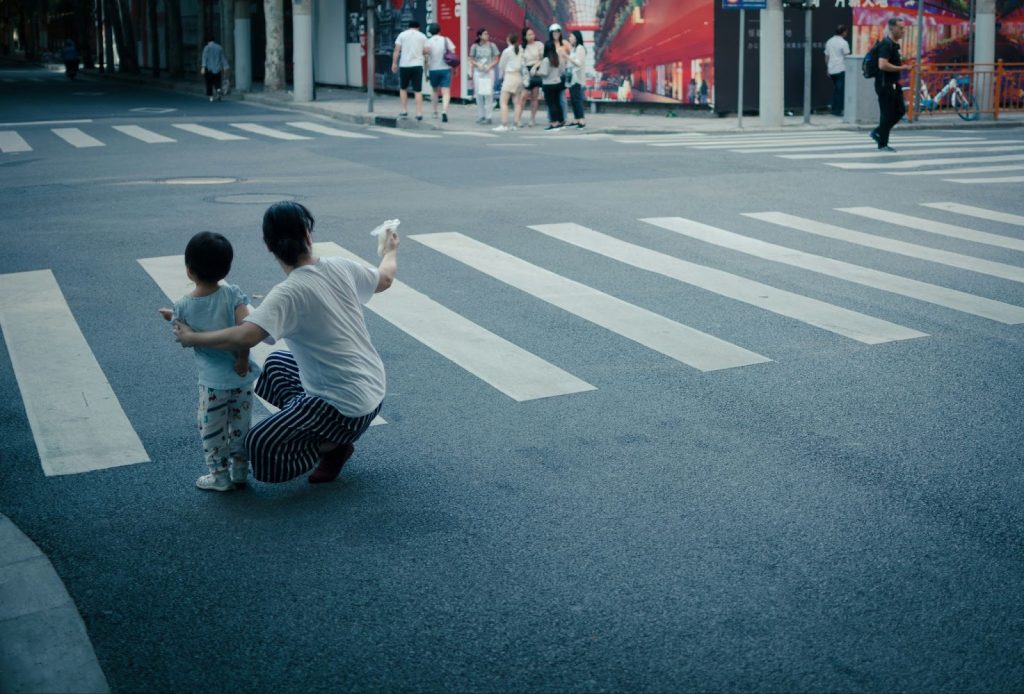 A mom and her child in the street near a crosswalk in a city intersection. The mom is pointing and explaining something. Illustrating holding boundaries while parenting post-Mormon from unconditional love.