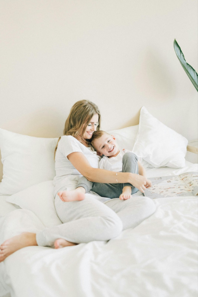 A smiling mom resting on the the bed with her smiling son. 