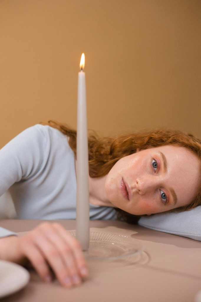 A woman taking a quiet moment with her head resting on her arm gazing at the camera with a candle in front of her. Illustrating taking time for ourselves as post-Mormon parents.