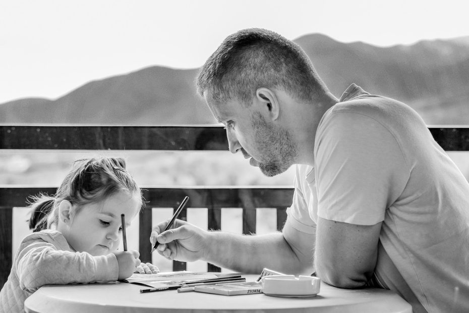 A dad and 5 year old daughter sitting at a balcony table writing in a workbook. Illustrating post-Mormon parenting with unconditional love and boundaries.