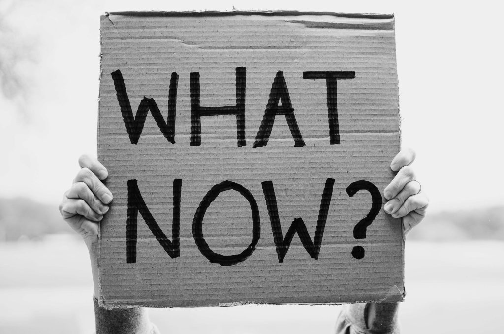 A person holding a piece of cardboard with the words "What Now?" written large in sharpie. Illustrating the feeling that there would be no life after leaving the LDS church.